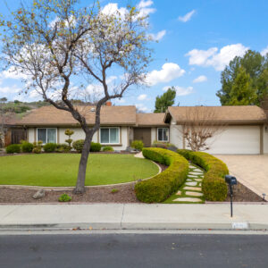this image shows the front yard, driveway and hedge lined stone walkway leading to the homes entry.